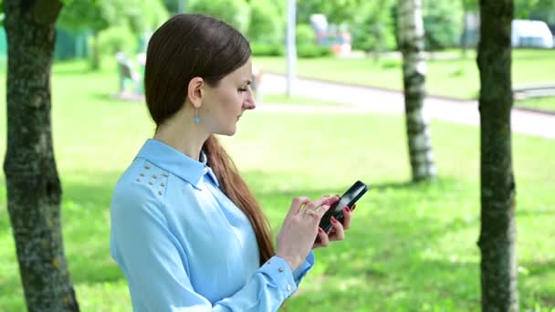 Βίντεο Καυκάσια μελαχρινή κοπέλα με μακριά μαλλιά μιλάει στο τηλέφωνο στο πάρκο. — Αρχείο Βίντεο