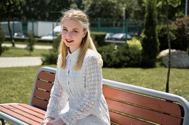 Bir bankta poz veren ve açık havada gülümseyen bir model. Parkta güzel bir sarışının fotoğrafı mutluluğu gösterir..