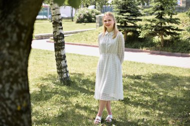 Açık havada güneşli bir havada gülümseyerek poz vermek. Parkta güzel bir sarışının fotoğrafı mutluluğu gösterir..