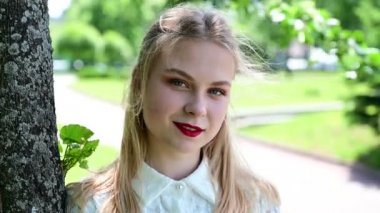 Güneşli havalarda poz veren makyajlı bir kız. Parkta gülümseyen güzel bir sarışının videosu.