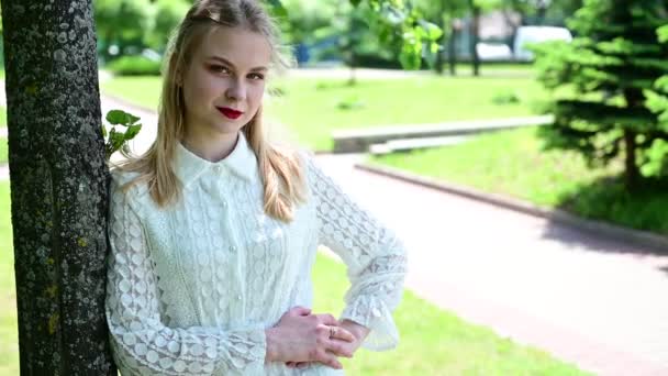 Mädchen mit tollem Make-up posiert bei sonnigem Wetter. Video einer hübschen Blondine in einem Park mit einem Lächeln. — Stockvideo