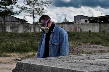 Gaz maskeli bir adam harabeler ve dramatik gökyüzü arkaplanı arasında yürüyor. Biyolojik tehlike kavramı. Çevre kirliliği, ekolojik felaket, radyasyon.