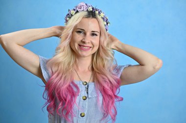 Kafasında çelenk olan güzel beyaz bir kadının yatay yakın plan portresi. Stüdyoda mavi arka planda gülümseyen sarı saçlı model.