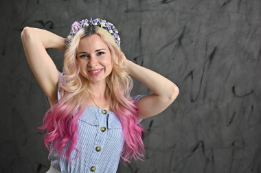 Kafasında çelenk olan güzel beyaz bir kadının yatay portresi. Sarı saçlı, sarışın model. Stüdyoda gri arka planda gülümsüyor.