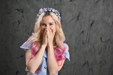 Stüdyoda gri arka planda gülümseyen sarışın model. Kafasında çelenk olan güzel beyaz bir kadının yatay portresi.