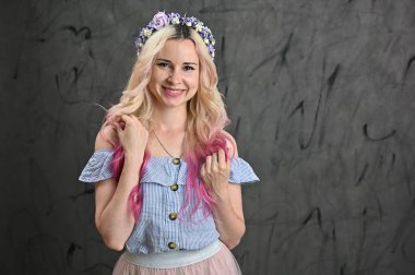 Stüdyoda gri arka planda gülümseyen sarışın model. Kafasında çelenk olan güzel beyaz bir kadının yatay portresi.