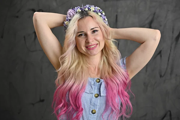 Stüdyoda gri arka planda gülümseyen sarışın model. Kafasında çelenk olan güzel bir kadının yatay portresi.