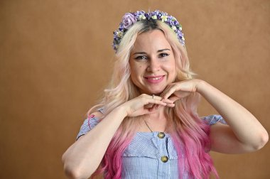 Stüdyoda bej arka planda poz veren sarı saçlı bir model. Kafasında çelenk olan güzel bir kadının yatay portresi..