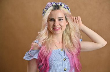 Stüdyoda bej arka planda poz veren sarı saçlı bir model. Kafasında çelenk olan güzel bir kadının yatay portresi..