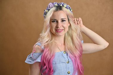 Kafasında çelenk olan güzel bir kadının yatay portresi. Stüdyoda bej arka planda gülümseyen sarı saçlı model.