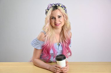 Stüdyoda beyaz arka planda gülümseyen çelenkli sarı saçlı manken. Elinde bir fincan kahve olan güzel bir kadının portresi.