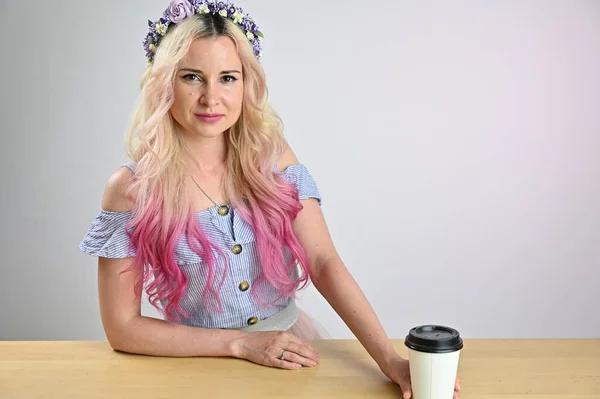コーヒーを片手にきれいな女性の肖像画 ブロンド色の髪モデルともに花輪笑顔ポージングでスタジオ上の白い背景 — ストック写真