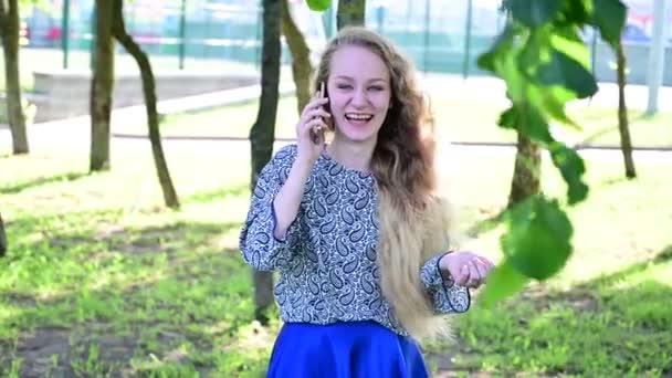 Den blonda flickan skrattar glatt och smittsamt när hon pratar på smarttelefonen. — Stockvideo