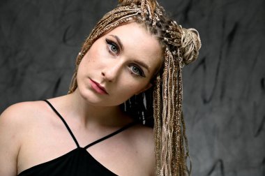 Gri arka planda poz veren güzel bir model. Stüdyoda uzun saçlı rastalı beyaz bir kadının yakın plan portresi.