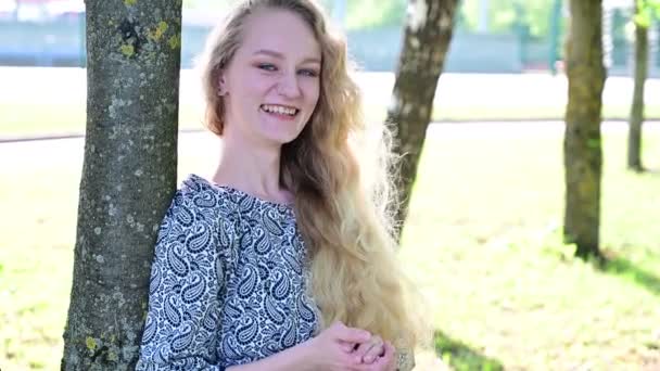 Ένα νεαρό γοητευτικό κορίτσι με όμορφα μαλλιά σε ένα καλοκαιρινό πάρκο γελάει χαρούμενα. — Αρχείο Βίντεο