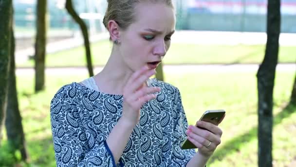 Menina incrível dizendo uau e sorrindo ao verificar o feed de notícias em pé no parque . — Vídeo de Stock