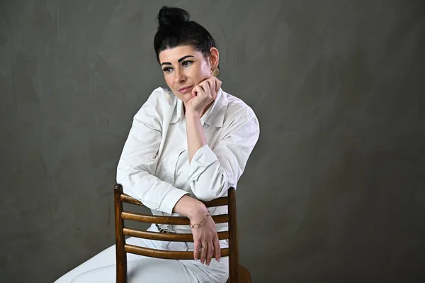 Portrait studio élégant d'une femme brune caucasienne assise sur une chaise sur un fond gris — Photo