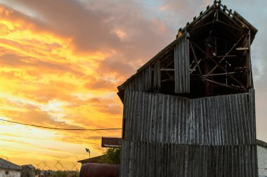 Sonbaharda terk edilmiş eski binaların fotoğrafı portakal rengi güneşin altında dramatik bir gökyüzünün arka planına karşı.