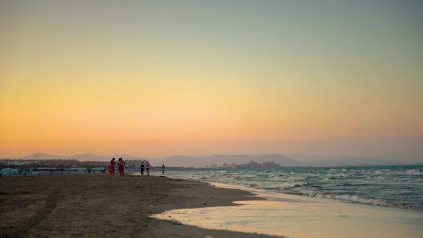 Light waves and people gather after swimming in front of the sunset on the beach of Malvarros. Valencia, Spain — Stock Video