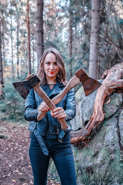 年轻美丽的妇女在皮革夹克与斧头在森林 — 图库照片