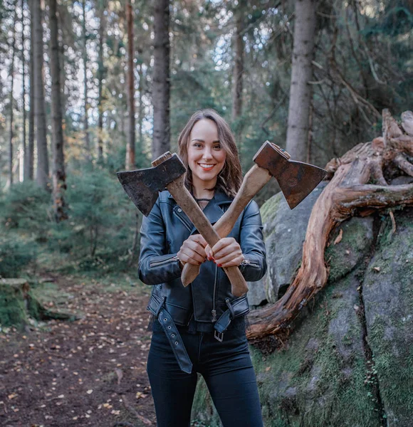 Joven hermosa mujer en chaqueta de cuero con hacha en un bosque — Foto de Stock