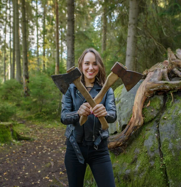 Молодая красивая женщина в кожаной куртке с топором в лесу — стоковое фото