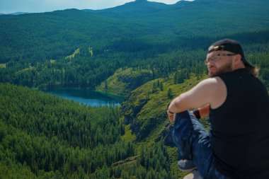 Dağların zirvesinde sırt çantalı ve güneşli bir günde güzel dağlarda duran sportif adam..