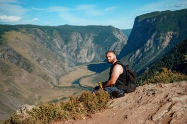 Dağların zirvesinde sırt çantalı ve güneşli bir günde güzel dağlarda duran sportif adam..