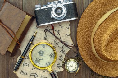 Şifreli bir mektup parçası, bir büyüteç, eski bir kamera, bir pusula, bir hasır şapka, eski bir defter, bir kalem ve bir cep saati. Hazine avı ve arkeolojik araştırma. Yukarıdan görünüşü