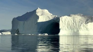 The huge sea white-blue iceberg and cave in still waters of Qarajaq Isfjord in Baffin Bay in summer. Unbelievable icy beauty. High quality movie.