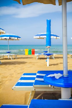 Bazı plaj şemsiyeleri ile bir plajda sarı, yeşil ve kırmızı renklerde üç çöp kutusu görünümü