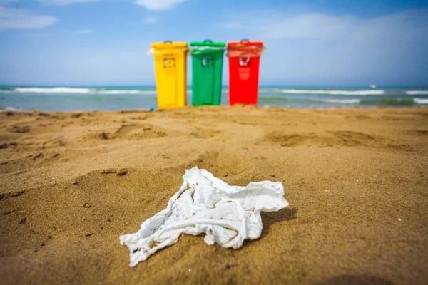 A view of three trash bin in yellow, green and red colours on a beach with some beach umbrellas