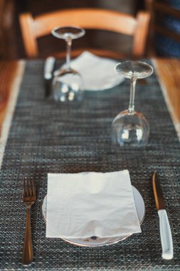 Açık ahşap masa ayarı: beyaz tabaklar, salam, peynir, asma ve jambon ile rustik koyu masa örtüsü. Üstte görüntü.