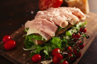 Ahşap arka planda peynir, jambon, salata, domates ve parmesan ile geleneksel İtalyan sandviç