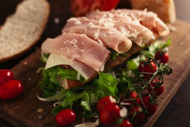 Ahşap arka planda peynir, jambon, salata, domates ve parmesan ile geleneksel İtalyan sandviç