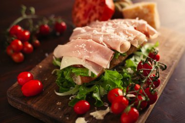 Ahşap arka planda peynir, jambon, salata, domates ve parmesan ile geleneksel İtalyan sandviç