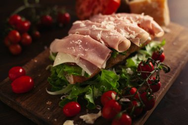 Ahşap arka planda peynir, jambon, salata, domates ve parmesan ile geleneksel İtalyan sandviç