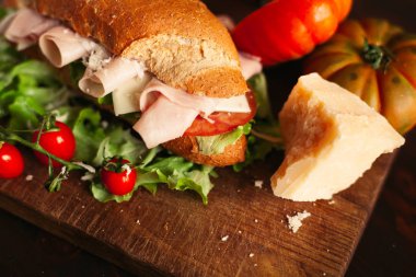 Ahşap arka planda peynir, jambon, salata, domates ve parmesan ile geleneksel İtalyan sandviç