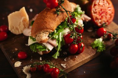 Ahşap arka planda peynir, jambon, salata, domates ve parmesan ile geleneksel İtalyan sandviç