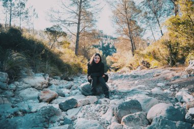 Gülümseyen kız dağ taş yol üzerindeki bir kayaya oturan kamera bakıyor