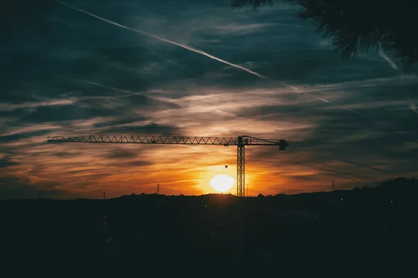 Sunset with blue and orange clouds with the silhouette of a construction crane in the center