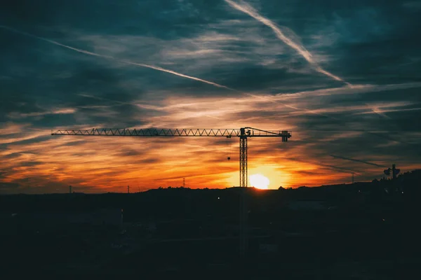 Sunset with blue and orange clouds with the silhouette of a construction crane in the center