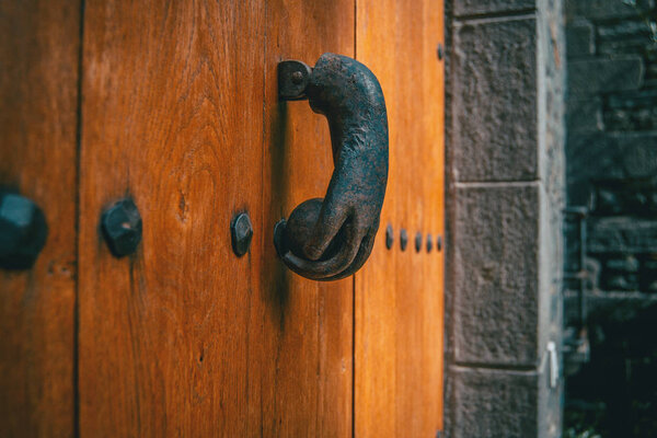 An old metal knocker shaped like a hand on a wooden door of a medieval village