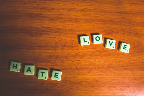 Love and hate spelled out with scrabble pieces on a wooden table