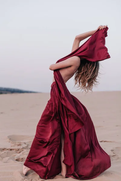 Fille avec un tissu rouge dans les rayons du coucher du soleil dans le désert — Photo