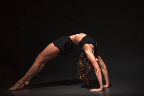 Siyah arka planda yoga yapan genç bir kız.