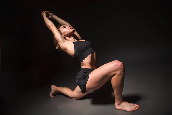 Siyah arka planda yoga yapan genç bir kız.