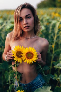 Genç üstsüz bir kız ayçiçeklerinde duruyor.