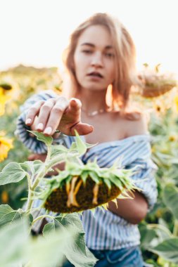 Tişörtlü genç bir kız ayçiçeklerinin içinde duruyor.