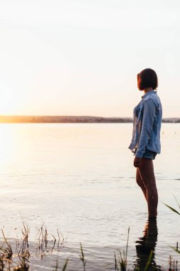 Genç bir kız gün batımının arka planında sahilde duruyor.. 